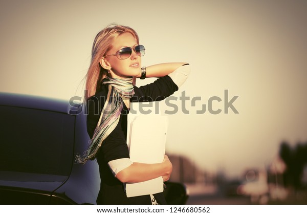 Fashion\
business woman with financial papers next to her car Stylish female\
model wearing black blazer and sunglasses\
outdoor