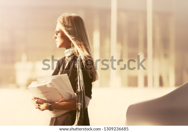 Fashion\
business woman with financial papers next to her car Stylish female\
model wearing dark blue blazer and\
sunglasses