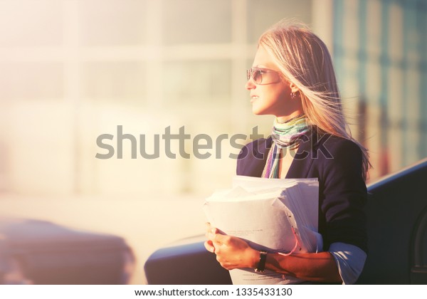 Fashion business\
woman with financial papers on city street Stylish female model in\
dark blue blazer and\
sunglasses