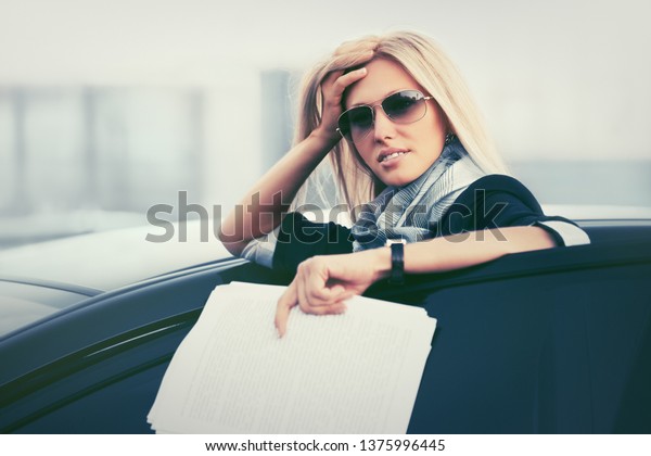 Fashion\
business woman with financial papers leaning on her car  Stylish\
female model in dark blue blazer and\
sunglasses