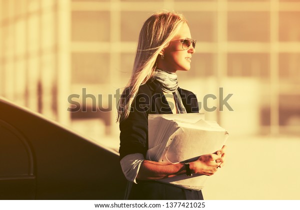 Fashion business\
woman with financial papers on city street Stylish female model in\
dark blue blazer and\
sunglasses