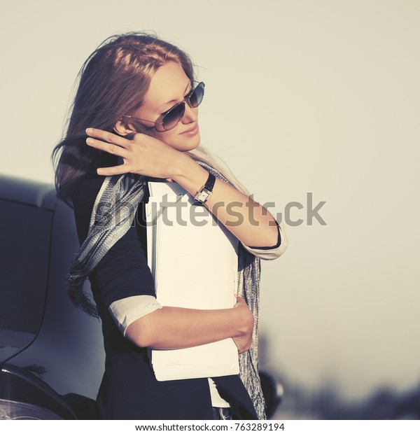 Fashion business woman\
with financial papers next to her car. Stylish female model in\
sunglasses outdoor