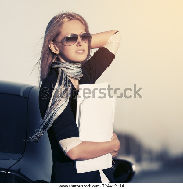 Fashion business woman\
with financial papers next to her car  Stylish female model in\
sunglasses outdoor