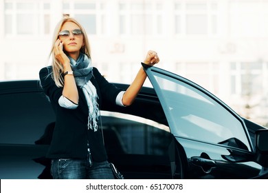 Fashion Businesswoman Calling On Cell Phone Outside A Her Car Stylish Female Model Wearing Sunglasses Black Suit Jacket And Blue Scarf