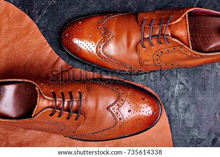 Fashion classical polished men's brown oxford brogues on piece of leather dark wooden background.Top view.