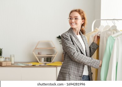 Fashion Closet Concept. Happy stylish girl in glasses choosing designer clothing on hangers, copy space - Powered by Shutterstock