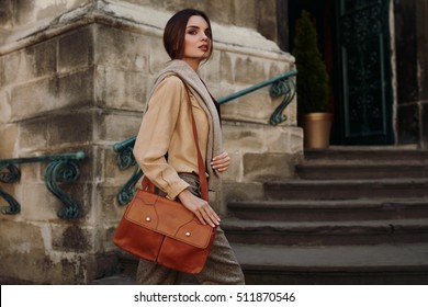 Fashion Clothes. Beautiful Sexy Woman Wearing High Fashionable Spring, Fall Clothing ( Shirt, Scarf, Pants, Sweater, Leather Bag ) Outdoors. Female Model In Trendy Outfit Posing In The Street