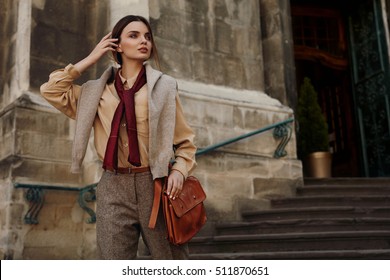 Fashion Clothes. Beautiful Sexy Woman Wearing High Fashionable Spring, Fall Clothing ( Shirt, Scarf, Pants, Sweater, Leather Bag ) Outdoors. Female Model In Trendy Outfit Posing In The Street