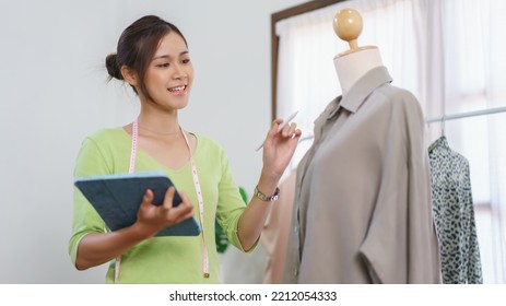 Fashion Clothes Merchant Concept, Female Designer Checks Detail Of Clothes And Take Notes On Tablet.