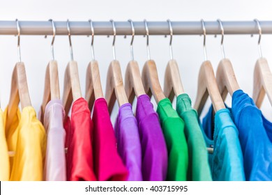 Fashion clothes on clothing rack - bright colorful closet. Closeup of rainbow color choice of trendy female wear on hangers in store closet or spring cleaning concept. Summer home wardrobe.