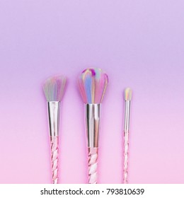 fashion colored makeup brushes on a gradient pink and purple background. pastel flat lay