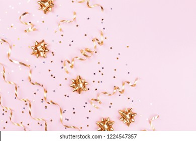 Fashion Composition With Golden Bows, Serpentine And Star Confetti On Pink Pastel Table Top View. Flat Lay Card For Birthday, Christmas Or Wedding.