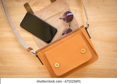 Fashion Concept : Flat Lay Of Brown Leather Woman Bag Open Out With Sunglasses And Smartphone On Wooden Background.