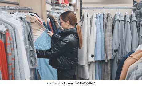 Fashion conscious shopper browsing clothing rack, carefully examining trendy garments and selecting stylish wardrobe piece
