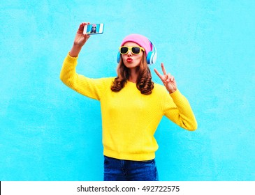 Fashion Cool Girl In Headphones Listening Music Taking Photo Makes Self Portrait On Smartphone Wearing A Colorful Clothes Over Blue Background