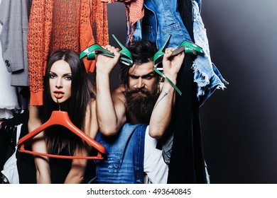 Fashion Couple Denuded Tired Of Brunette Girl With Red Hangers And Bearded Man With Green High Heels Shoes Among Clothes To Wear Near Rack In Closet
