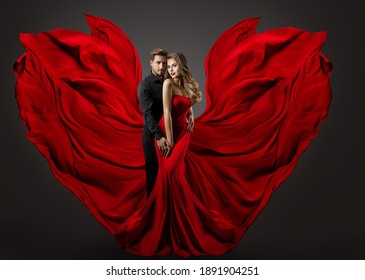 Fashion Couple In Love. Woman In Fantasy Long Red Gown And Handsome Man. Flying Silk Fabric As Wings. Studio Portrait