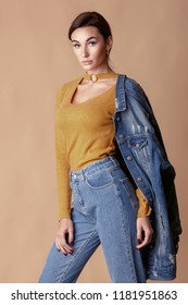 Fashion Denim Look. Young Beautiful Woman Over Beige Background In Mom Jeans And Oversize Demin Jacket. 90s Style.