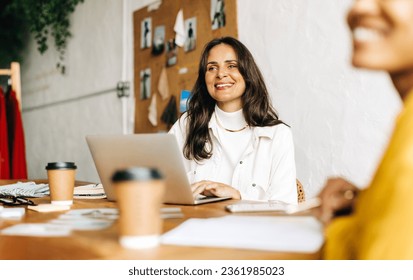 Fashion design team working in their office, sitting at their desks and engaging in a discussion with a client. Female entrepreneurs using their creativity to build a clothing design business. - Powered by Shutterstock