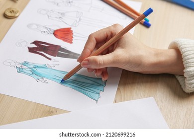 Fashion Designer Creating New Clothes In Sketchbook At Wooden Table, Closeup