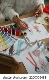 Fashion Designer Creating New Clothes In Sketchbook At Wooden Table, Closeup