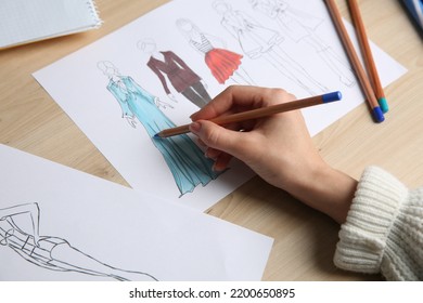 Fashion Designer Creating New Clothes In Sketchbook At Wooden Table, Closeup