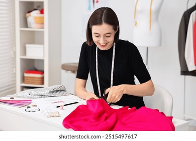 Fashion designer cutting pink fabric at table in workshop - Powered by Shutterstock