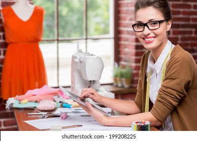 Fashion designer with digital tablet. Beautiful young woman working on digital tablet and smiling while sitting at her working place  - Powered by Shutterstock