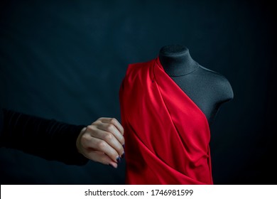 Fashion designer hand touching with clothing mannequin dummy with orange drape folding down in the studio with black background