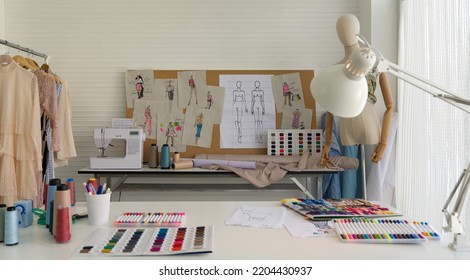Fashion designer room. Sewing Machine and various sewing related items on the table. Mannequins standing, colorful fabrics and a clothes rack with various kind of dress place beside the table. - Powered by Shutterstock