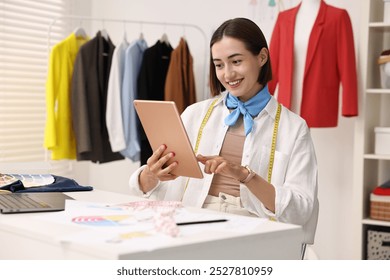 Fashion designer using tablet at table in workshop - Powered by Shutterstock