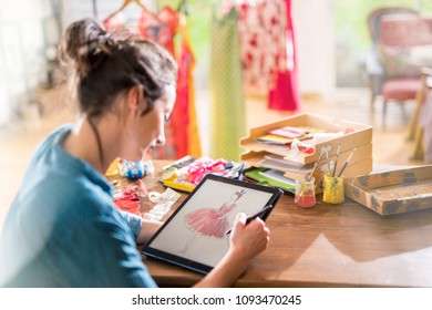 Fashion designer working on a new model in her studio, she designs a new dress on a digital tablet - Powered by Shutterstock