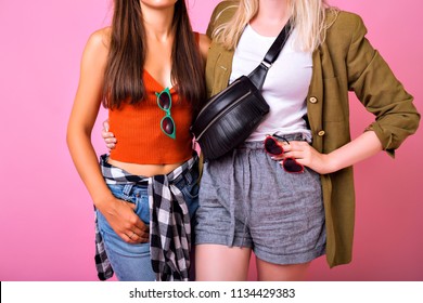 Fashion Details Stylish Picture, Two Woman Hugs And Posing Together In Studio, Casual Trendy 90s Style Outfits, Jeans, Crop Top, Plated Shirt, Vintage Jacket, Bum Bag And Sunglasses.