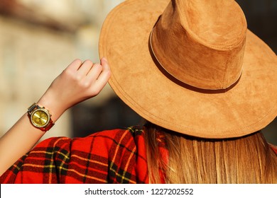 Fashion details: woman wearing suede light brown hat, golden wrist watch, red tartan scarf. Autumn street style concept