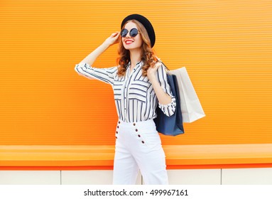 Fashion Elegant Young Smiling Woman Model With Shopping Bags Wearing A Black Hat White Pants Over Colorful Orange Background