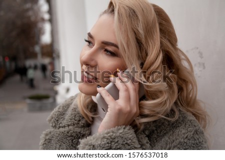 Fashion european woman walking at the street, dressed modern clothes. Female moder wearing faux fur coat, tutleneck, skirt, and curl hairstyle. woman talking on the phone