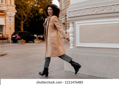 Fashion  full length  image of elegant  black woman in stylish luxury beige coat and velvet sweater, hight heels, walking outdoor. 