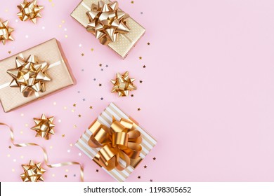 Fashion gifts or presents boxes with golden bows and star confetti on pink pastel table top view. Flat lay composition for birthday, christmas or wedding.