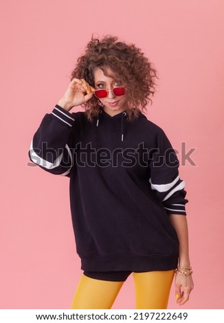 Fashion Girl with curly hair and colored make-up, sunglasses posing on a pink background