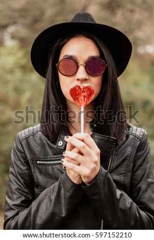 Fashion girl hipster with sunglasses and black leather jacket and a red candy