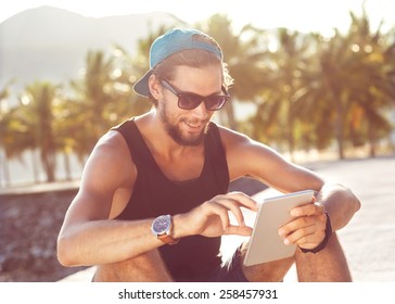 fashion guy sitting on the tablet, running in sunglasses on the beach with views of the mountains - Powered by Shutterstock