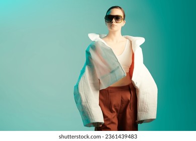 Fashion haute couture collection. Beautiful fashion model girl posing in designer clothes on blue studio background with place for text. Wide free forms in clothes, oversized style. 