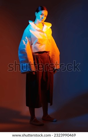 Fashion and haute couture style. Beautiful fashion model girl posing in stylish clothes with wide oversized shapes. Studio shot against a dark background in mixed color light. Bright colors.