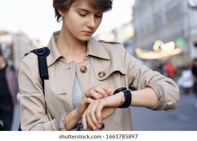 Fashion hipster millennial teen girl traveler using wrist smart watch walk on urban city street. Young woman traveler look at smartwatch digital modern tech app concept outdoor lifestyle. Closeup.