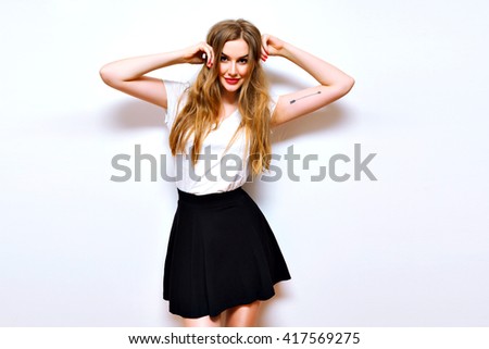 Fashion indoor portrait of hipster girl, amazing long blonde hairs, natural make up, simple casual black and white clothes, urban image with flash, white wall.