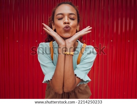Fashion, kiss and black woman being playful against a red wall in the city of Norway for travel. Face of a young, happy and pouting girl with luxury makeup, clothes and happiness on an urban holiday