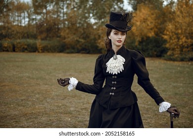 Fashion of the late 19th - early 20th century. A sophisticated brunette lady in a strict elegant black suit of the 19th century strolls through an autumn park.