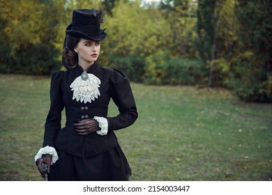 Fashion of the late 19th - early 20th centuries. A sophisticated brunette lady in a strict elegant black suit of the 19th century strolls through an autumn park. Copy space.