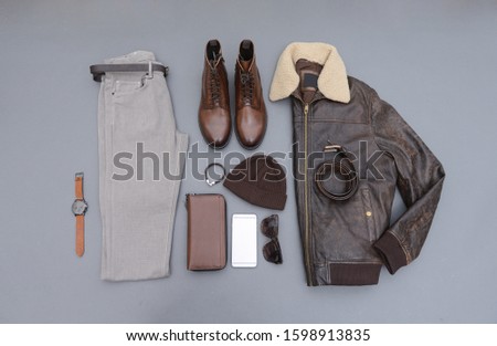 Fashion leather jacket with khaki pants and brown boots shoes,hat,watch, sunglasses,phone, isolated on gray background
