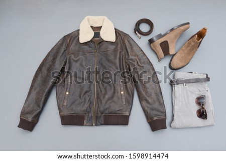 Fashion leather jacket with khaki pants and brown boots shoes,purse, scarf,sunglasses isolated on gray background
